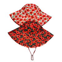 A reversible hat with patterns on each side. One side features red poppies with green leaves on a white background, while the other side has the same pattern on a black background. The hat has a wide brim and a red strap for securing it under the chin.