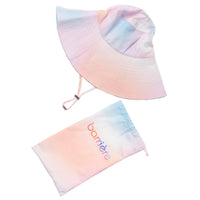 A pastel-colored bucket hat next to a matching gradient bag that transitions from pink to blue. The hat is made of soft fabric and features shades of pink, blue, and white.
