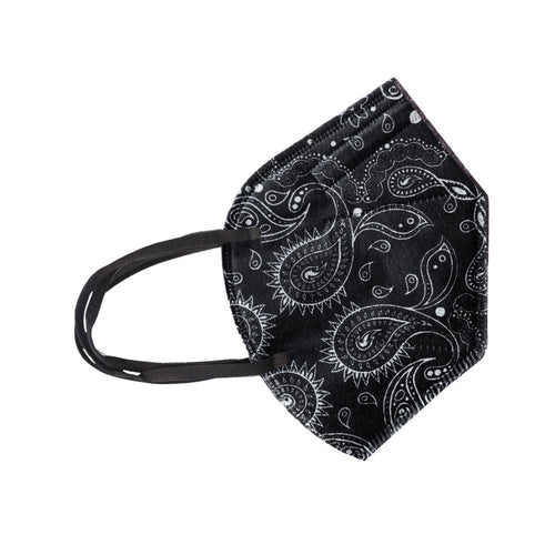 A black and white paisley face mask lying flat on a light plain surface. The mask has a contoured design with a prominent seam down the center and black elastic ear loops.