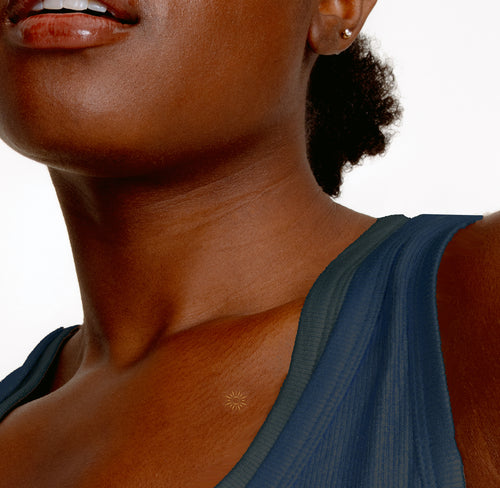 Close-up of a collarbone with a small adhesive patch with gold sun feature.