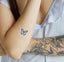 An individual wearing a half sleeve tattoo on the left hand with vitamin patch at the right forearm featuring blue-white-black butterfly.