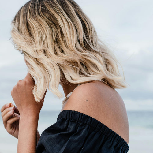An individual near the sea wearing a ‘CALL OF BEAUTY’ vitamin patch on their shoulder.