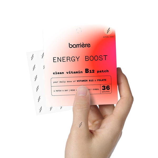 An individual hand holding the packet of 36 ‘ENERGY BOOST’ patches, with one patch on thumb of the right hand. The 36 patches are slightly visible, angled out from the side of the packaging.