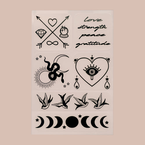 A collection of black vitamin patches on a beige background. There are six distinct designs, including symbols of love, strength, peace, and gratitude written in stylized text; two crossed arrows with a heart and infinity symbol; a sun with rays; an eye within a heart shape; two swallows facing opposite directions with stars between them; phases of the moon ranging from new to full moon; and various celestial bodies like stars, sun and moon, with love strength peace gratitude cursive text.