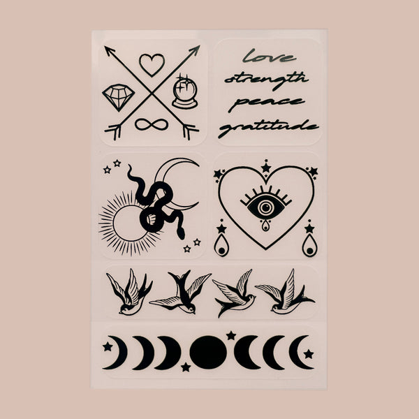 A collection of black vitamin patches on a beige background. There are six distinct designs, including symbols of love, strength, peace, and gratitude written in stylized text; two crossed arrows with a heart and infinity symbol; a sun with rays; an eye within a heart shape; two swallows facing opposite directions with stars between them; phases of the moon ranging from new to full moon; and various celestial bodies like stars, sun and moon, with love strength peace gratitude cursive text.