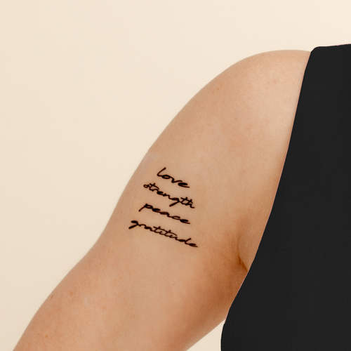 Person’s upper arm with a vitamin patch of four words written in cursive script: ‘love,’ ‘strength,’ ‘peace,’ and ‘gratitude.’