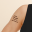 Person’s upper arm with a vitamin patch of four words written in cursive script: ‘love,’ ‘strength,’ ‘peace,’ and ‘gratitude.’