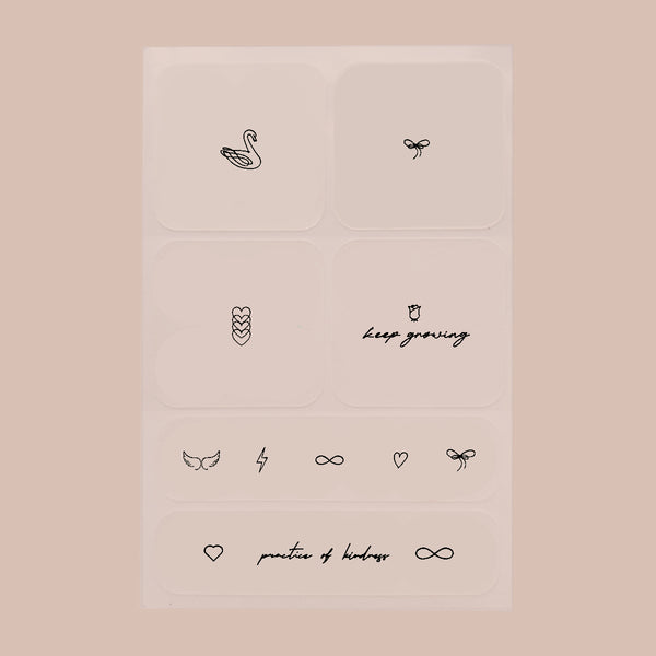 Six black patches with small prints on each, featuring designs ranging from swans to hearts to quotes, on a beige background.