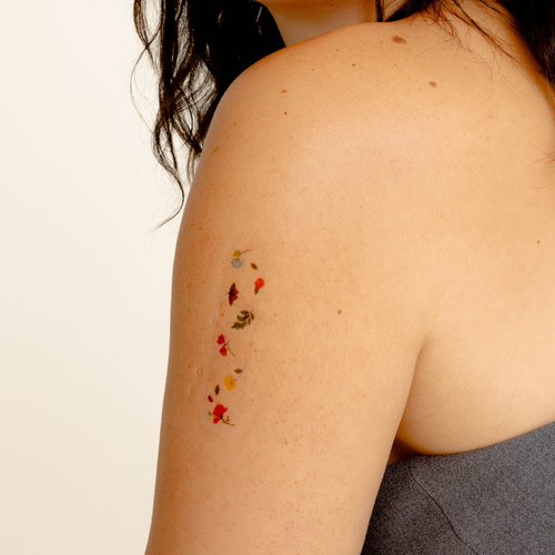 A person’s upper arm with a vitamin patch applied. The patch is small and has a translucent edge with colorful flowers printed. 