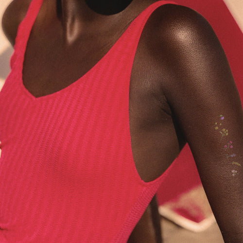 A person’s upper arm with a vitamin patch applied. The patch is small and has a translucent edge with colorful flowers printed. 