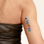 A person's arm with a vitamin patch featuring a palm tree, two birds and butterfly, a setting sun post cards.