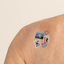 Close-up of an upper back shoulder with a 'Travel Well' vitamin patch of a cactus, three fishes, a three mountains and circle postcards.