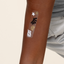 Close-up of an arm with a 'Travel Well'   vitamin patch with black, white and gold shell, star, sea weeds features.