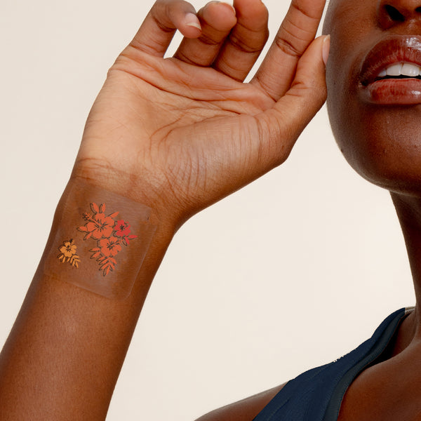 Close-up of a forearm with a temporary floral patch in shades of red and gold.